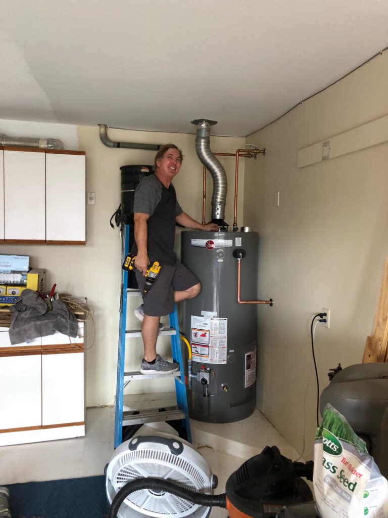 Eric Strand working from a ladder beside a gas water heater during installation
