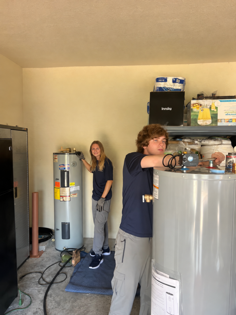 Two WHE crew members with tank water heaters during a garage installation project.