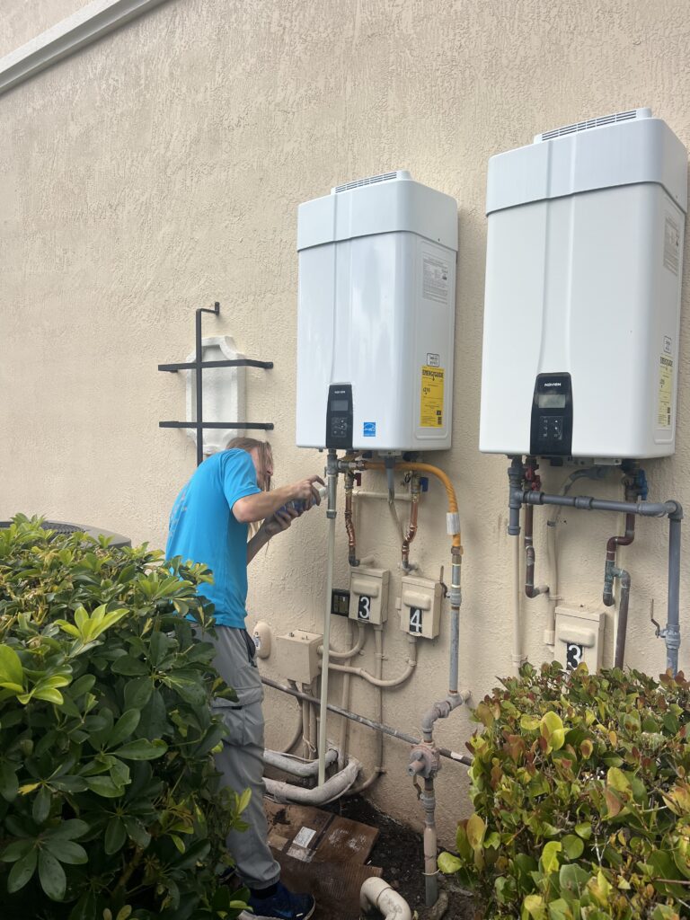 WHE team member working on connections beneath two outdoor Navien tankless water heaters