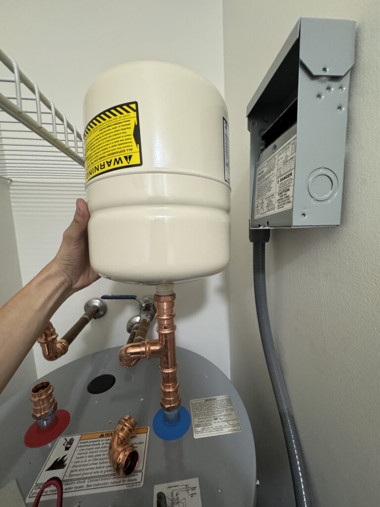 Installer positioning an expansion tank above an electric water heater during plumbing work